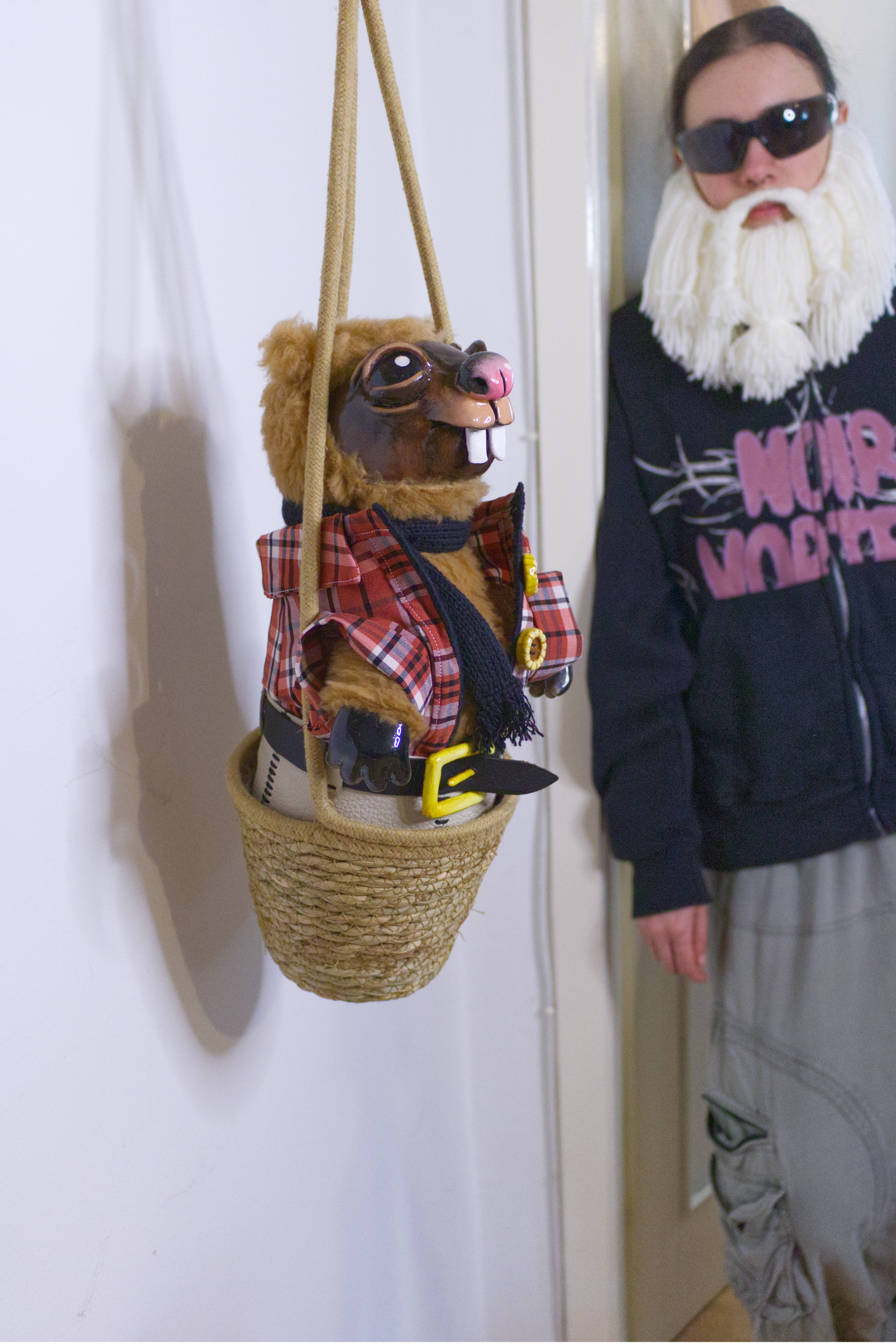 The Crafting Wizard wearing a beard, hat, and sunglasses stands behind a handmade marmot plush in traditional outfit with sculpted clay face and hands.