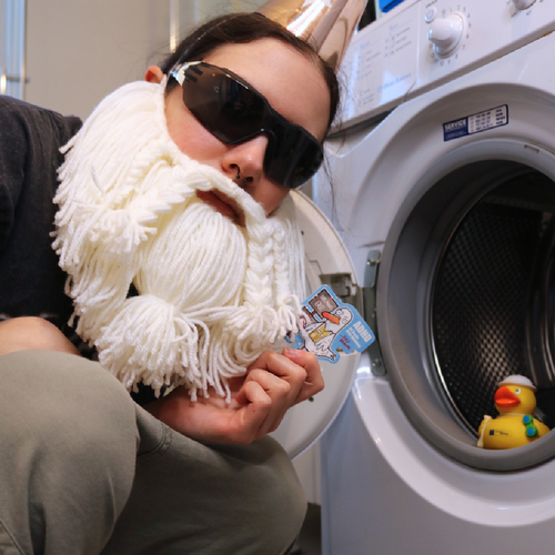 Sticker “ADHD - All Ducks Hate Dolphins” held by the Crafting Wizard squatting in front of an open washing machine with a rubber duck inside, shown in a funny staged scene.