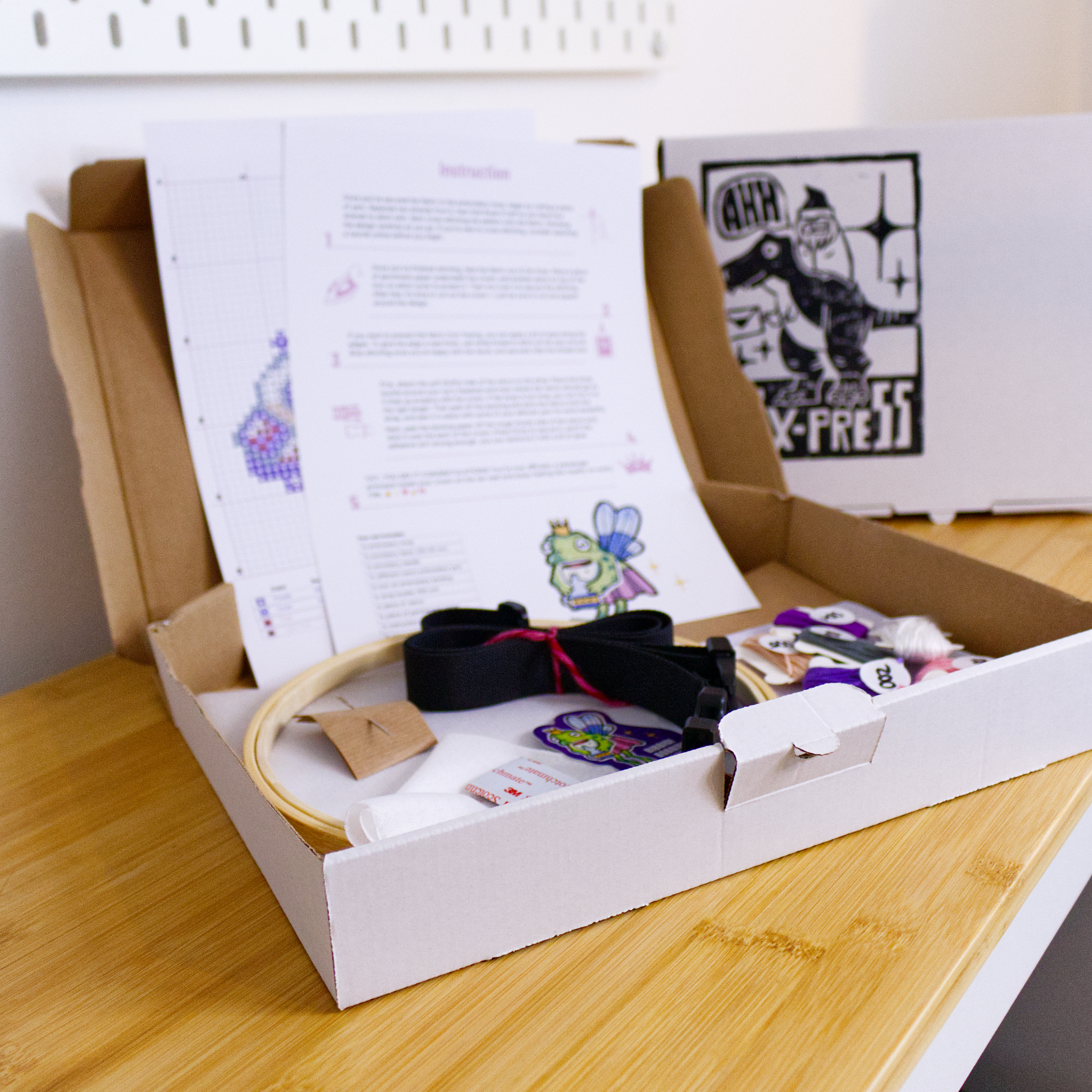 Open cross-stitch kit for the Barbie Passenger Princess crown displayed on a wooden table, showing embroidery hoop, threads, instructions, and pattern sheets.
