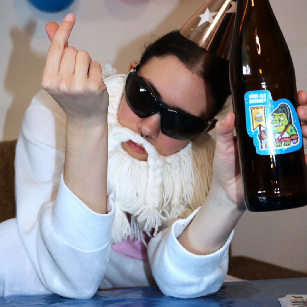Drunk Ogre Frog Sticker placed on a bottle, shown in a funny party scene with the Crafting Wizard at a kids birthday table, decorated with a colorful tablecloth and balloons in the background.