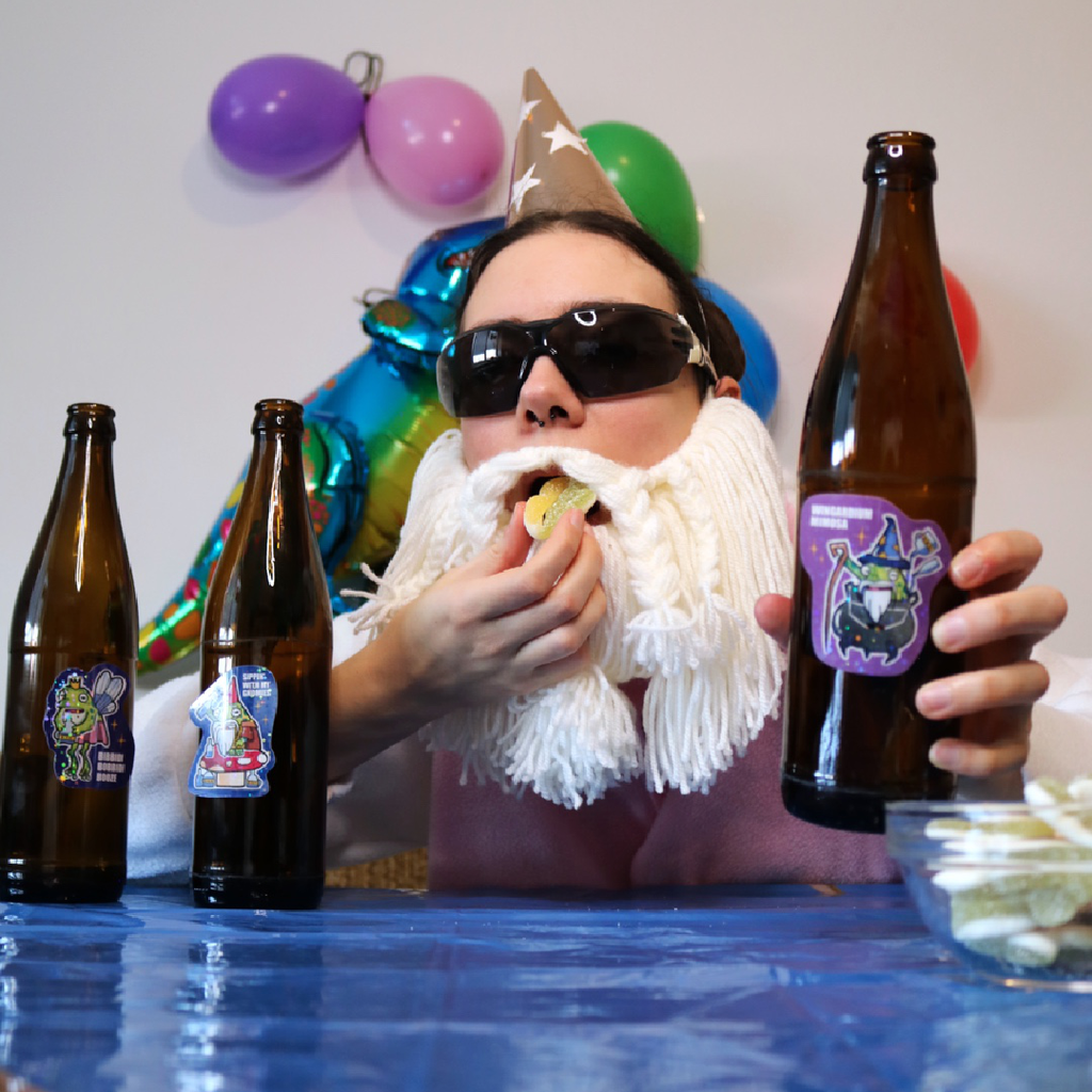 Drunk Wizard Frog Sticker placed on a bottle, shown in a funny party scene with the Crafting Wizard at a kids birthday table, decorated with a colorful tablecloth and balloons in the background.