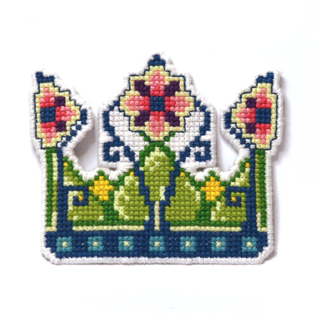 Cross-stitch fairy crown in green, blue, yellow, and pink with floral details.