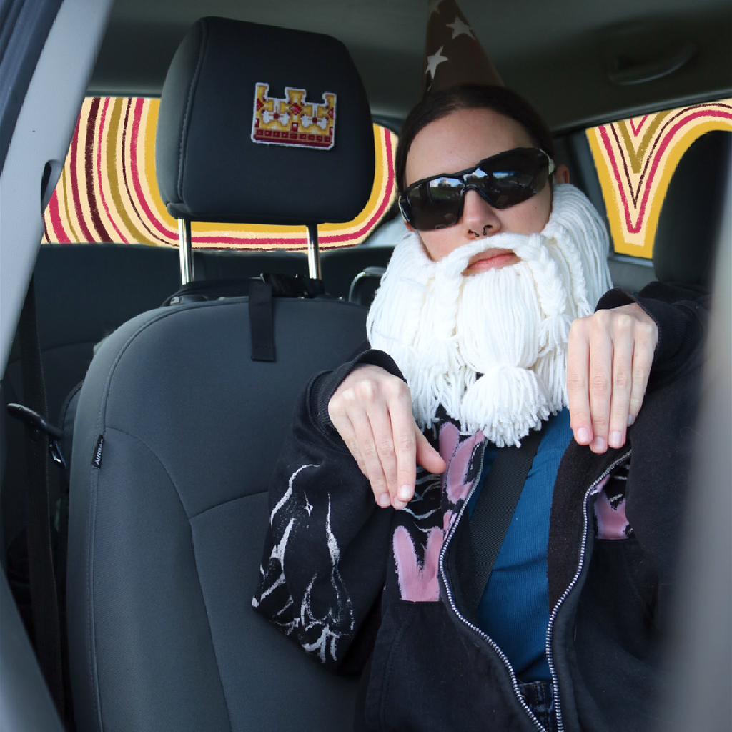 Cross-stitch King’s Crown placed on a car seat neck support for a “passenger princess” setup, with the Crafting Wizard present, a humorous staged scene.