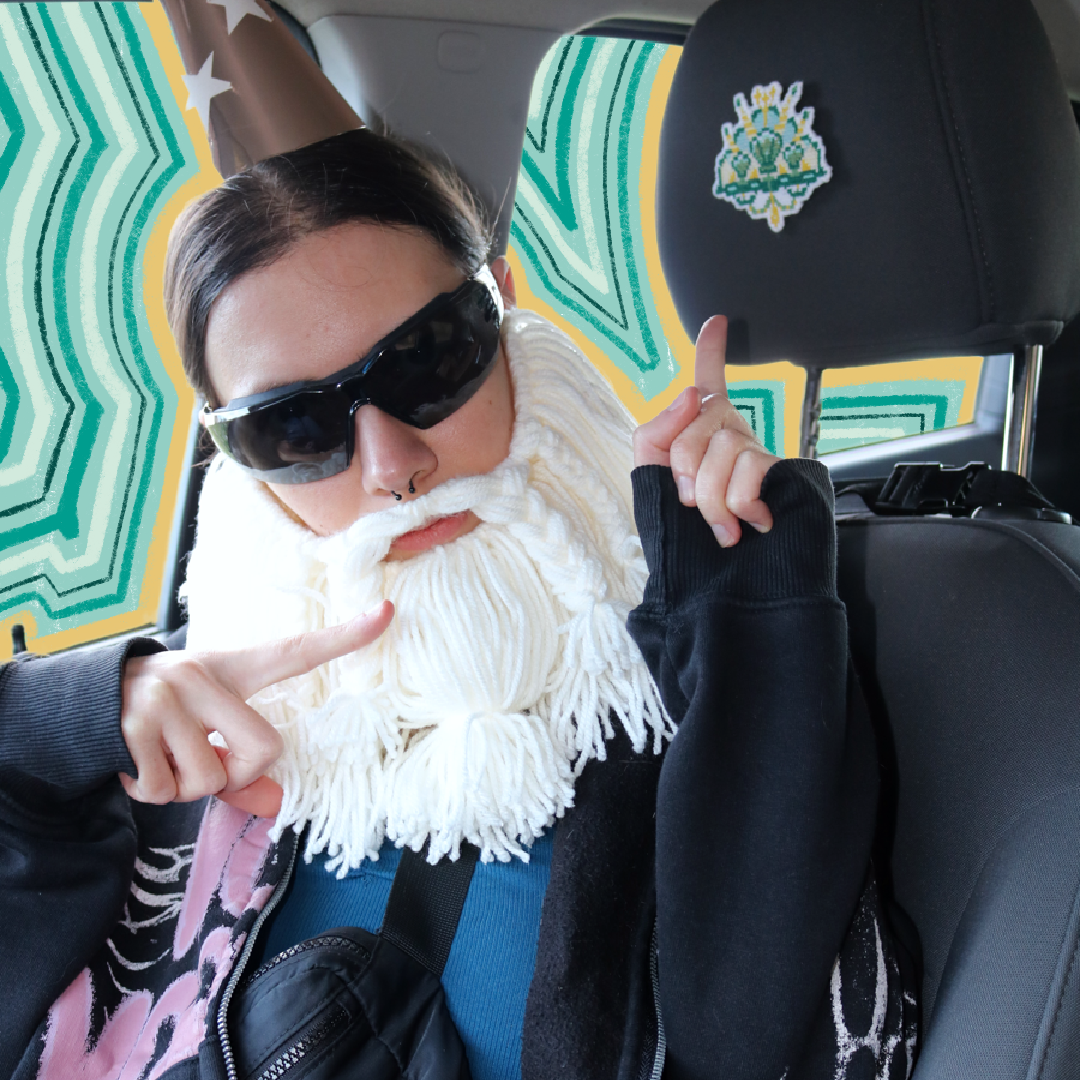 Cross-stitch Mermaid Crown placed on a car seat neck support for a “passenger princess” setup, with the Crafting Wizard present, a humorous staged scene.