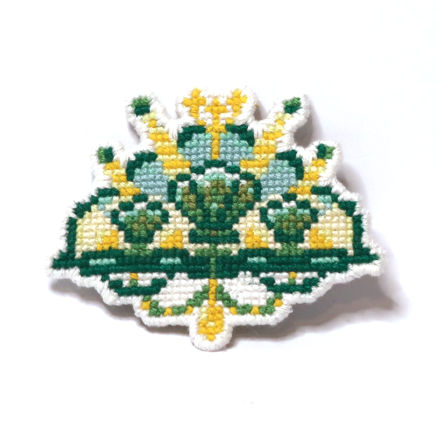 Cross-stitch mermaid crown in green and yellow with shells and a trident motif.