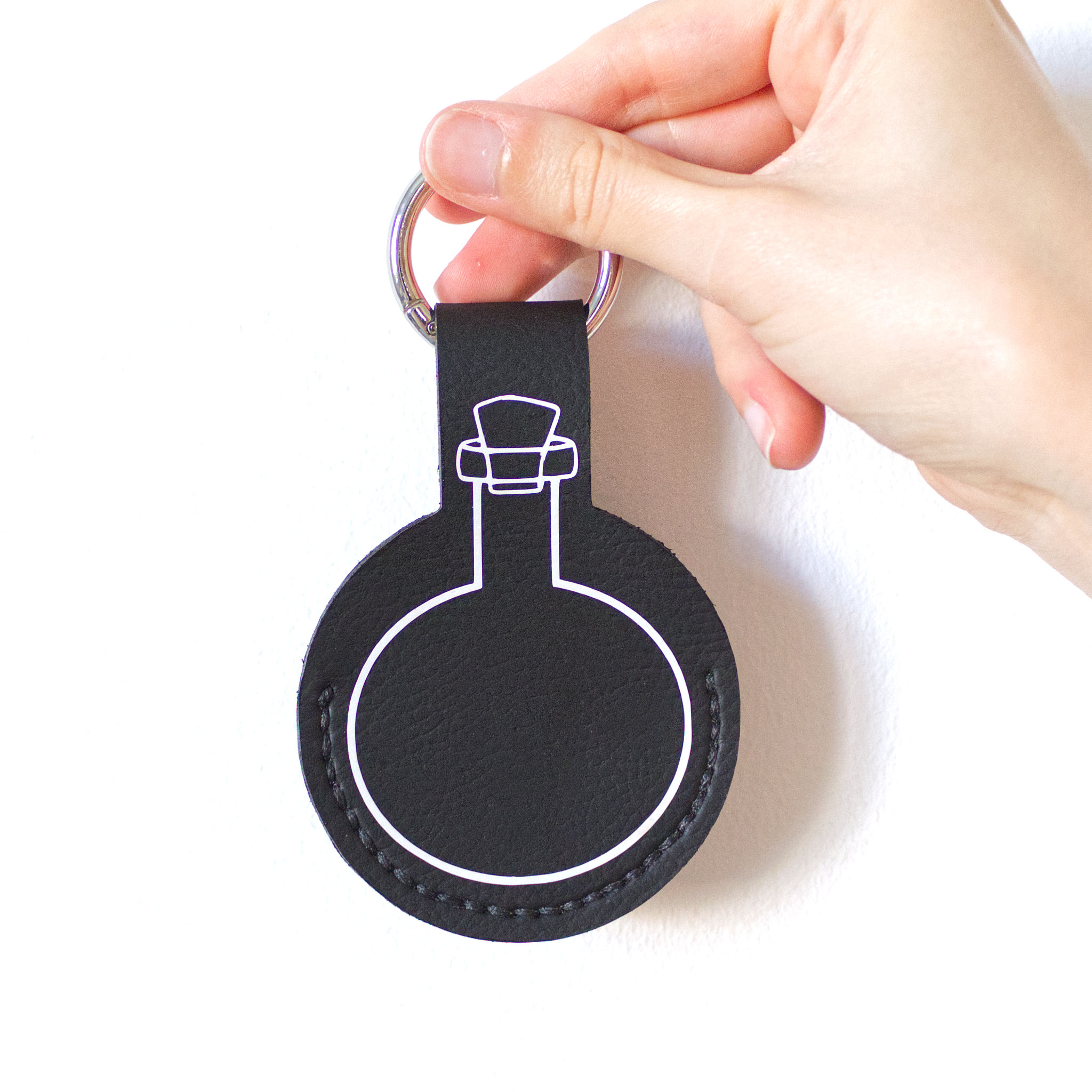 Black faux-leather potion keychain with stitched details, a potion bottle print, and a metal carabiner.