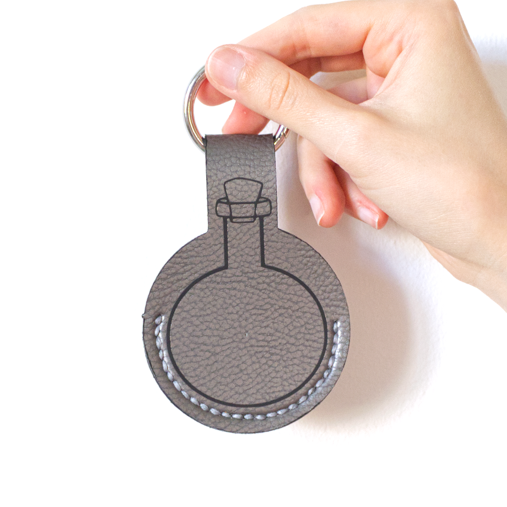 Grey faux-leather potion keychain with stitched details, a potion bottle print, and a metal carabiner.