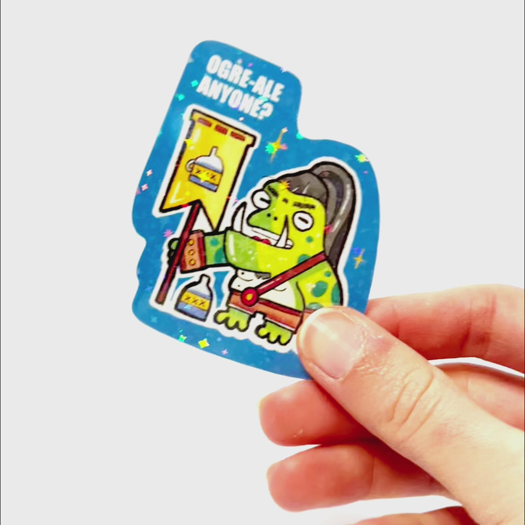 Video: Sticker of a drunk ogre frog with a ponytail holding a battle flag with a bottle, standing beside a bottle, with the slogan ‘Ogre-Ale Anyone?’