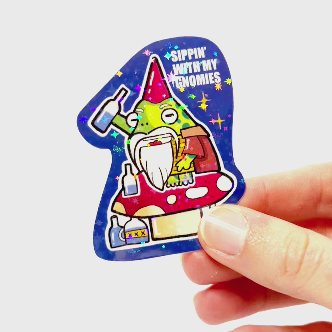 Video: Sticker of a drunk gnome frog sitting on a large mushroom, raising a bottle, with many bottles below and the slogan ‘Sippin’ With My Gnomies.’