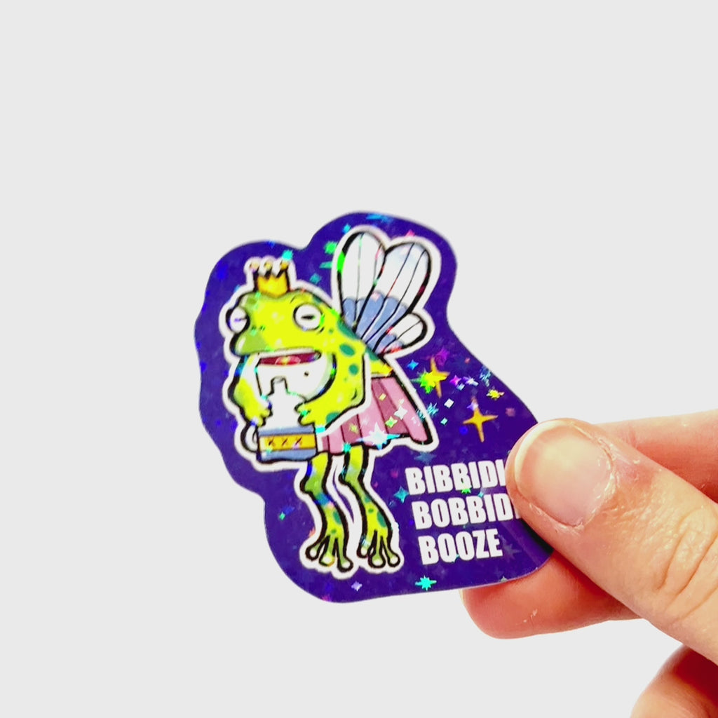 Video: Sticker of a drunk fairy frog with wings and a crown, holding a bottle and looking confused, with the slogan ‘Bibbidi Bobbidi Booze.’